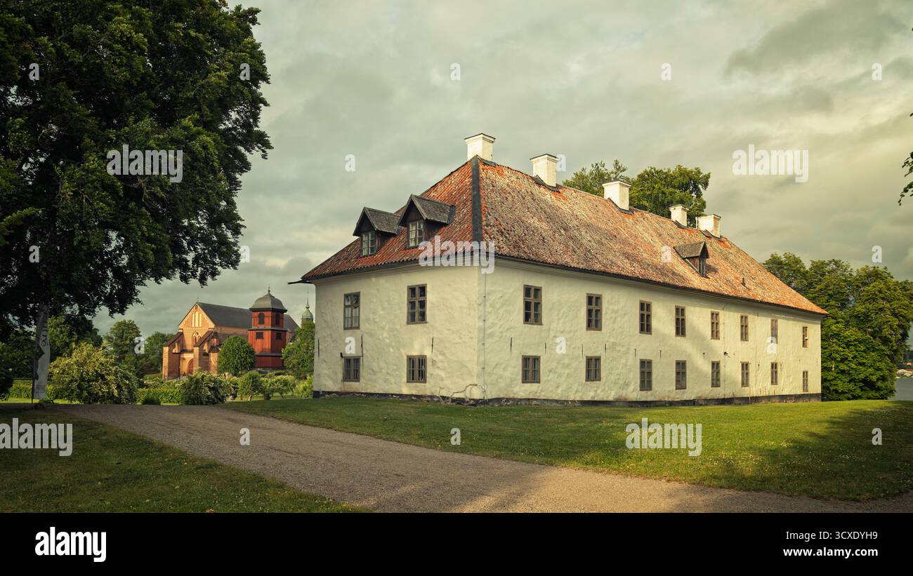 Blick auf das weiße Steinhaus und die rote mittelalterliche Skokloster-Kirche auf dem historischen Schlossgelände in Uppland, Schweden. Stockfoto