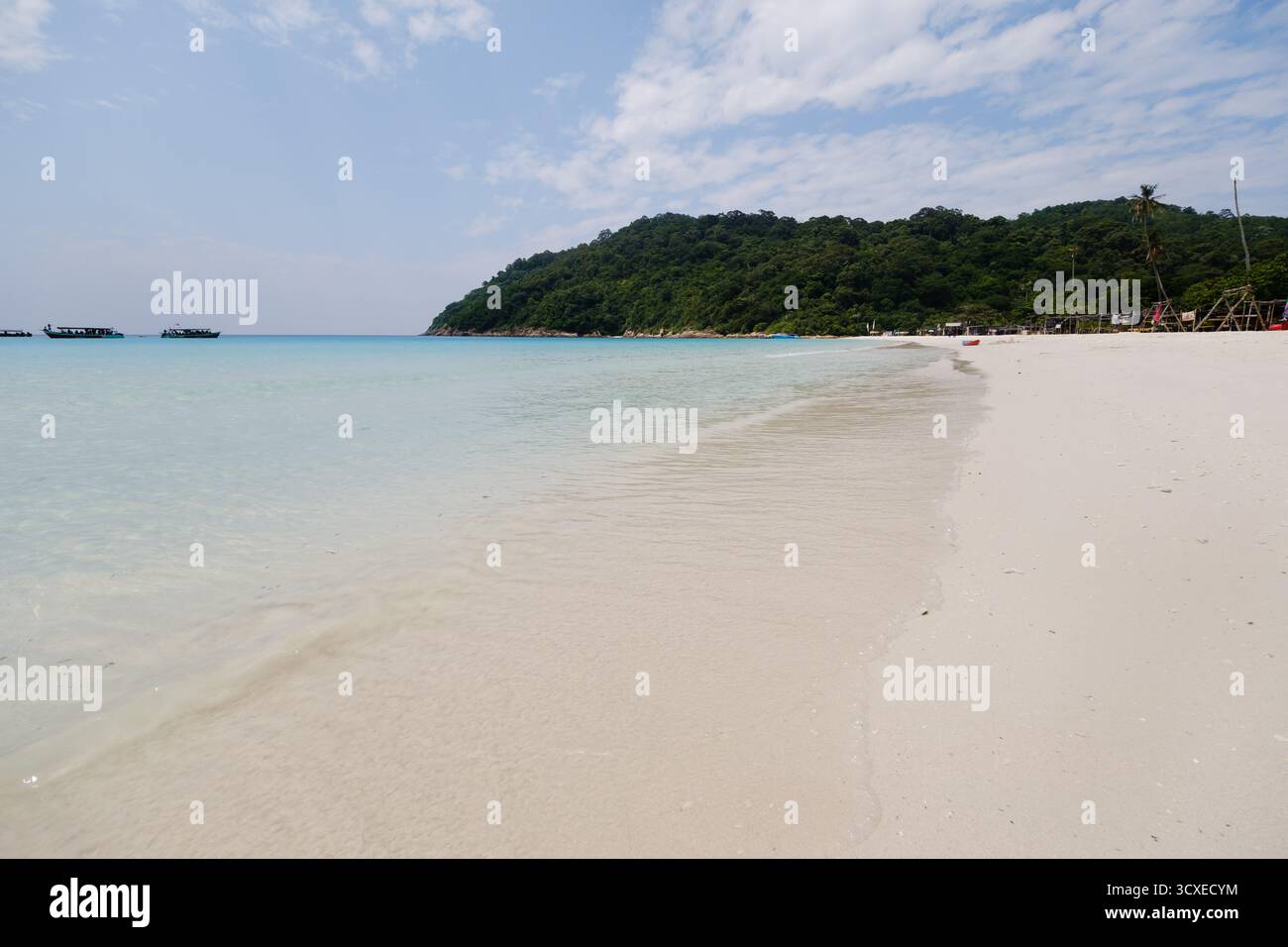 Die Wellen schlagen sanft gegen die Küste eines Sandstrandes, umgeben von üppigen grünen Hügeln. Das klare türkisfarbene Wasser glitzert unter dem Sonnenlicht und erzeugt einen Ser Stockfoto