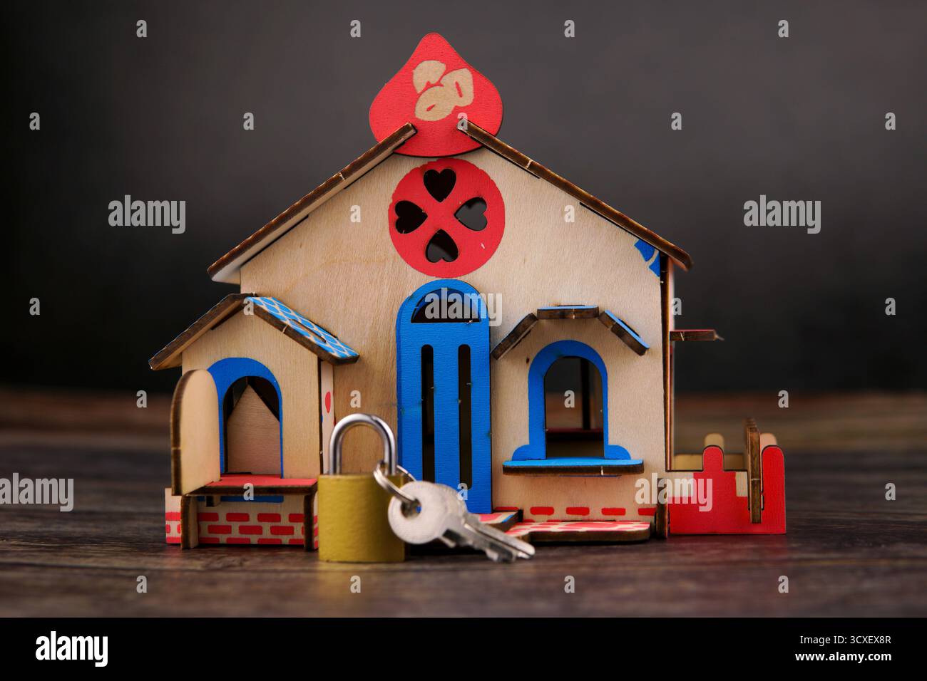 Mini-Holzhausmodell mit Vorhängeschloss und Schlüsseln vorne, symbolisiert Wohneigentum, Immobilieninvestition, Immobiliensicherheit. Stockfoto