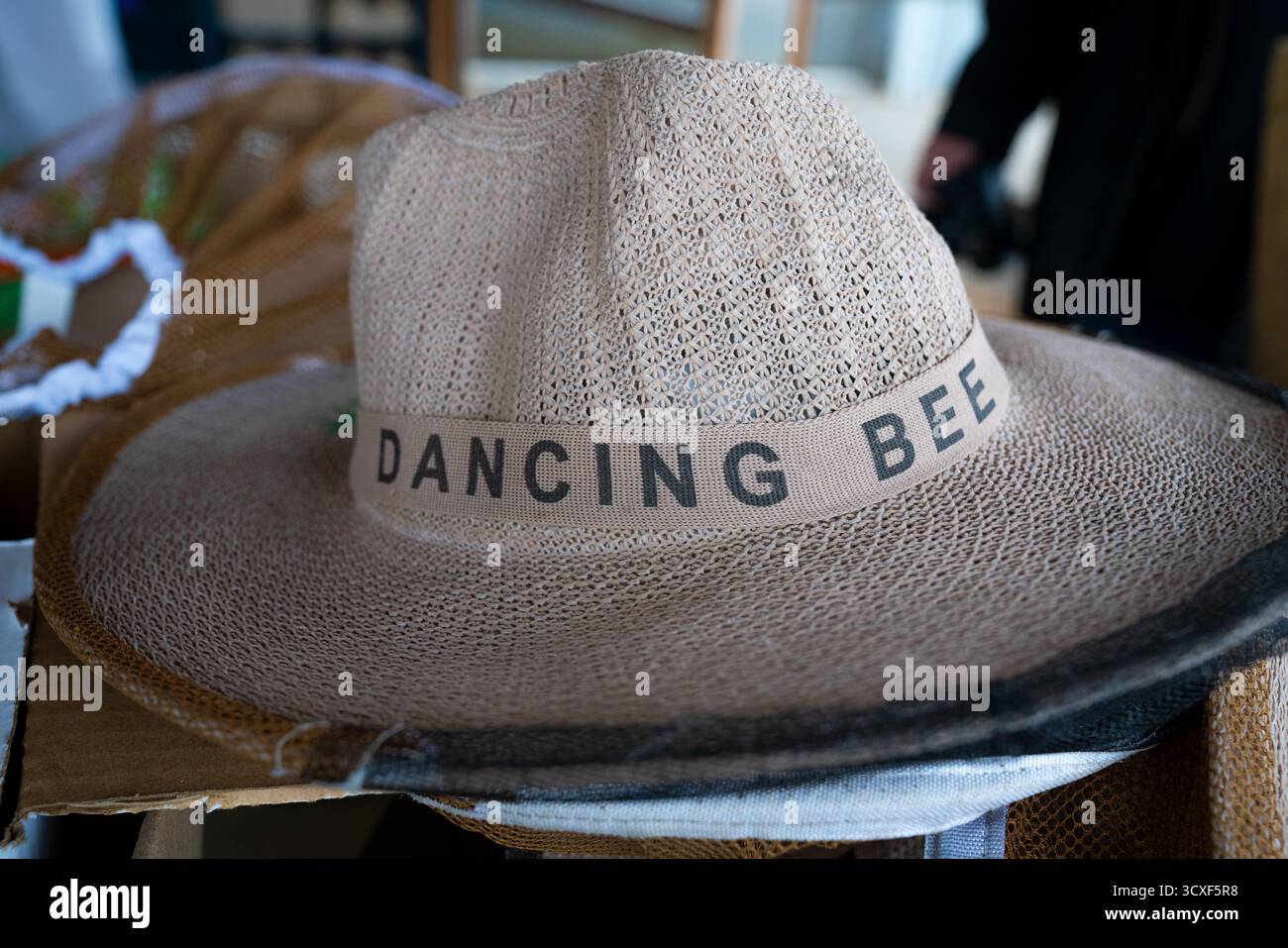 Nahaufnahme eines gewebten Bienenzuchtmutes mit dem Aufdruck „Dancing Bee“ auf der Band, der Handwerkskunst und Identität in der nachhaltigen Imkerei repräsentiert Stockfoto
