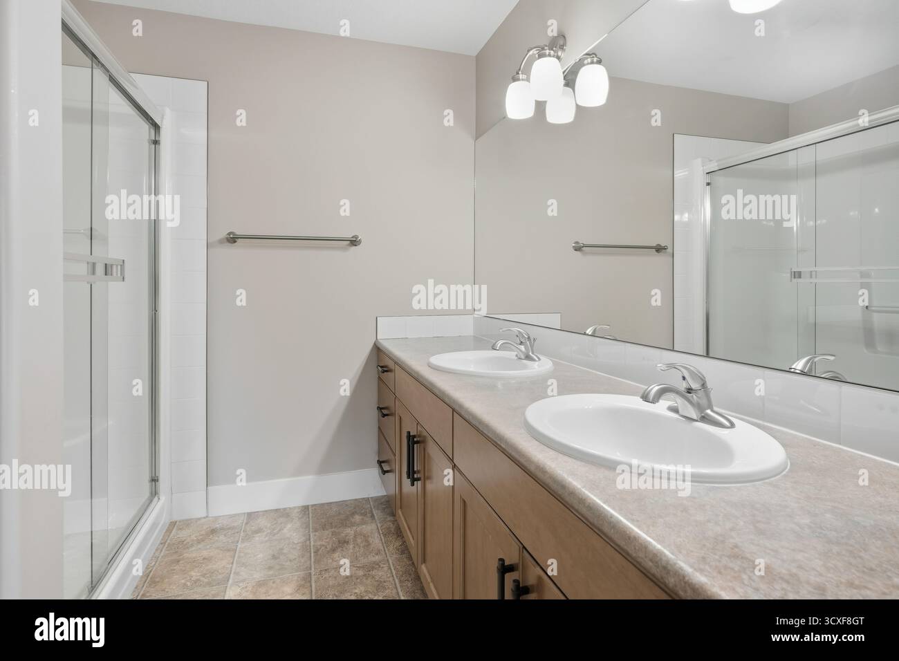Bad mit Dusche und zwei Waschbecken. Das Bad ist sauber und gut beleuchtet. Der Spiegel ist groß und reflektiert das Licht der Deckenleuchten Stockfoto
