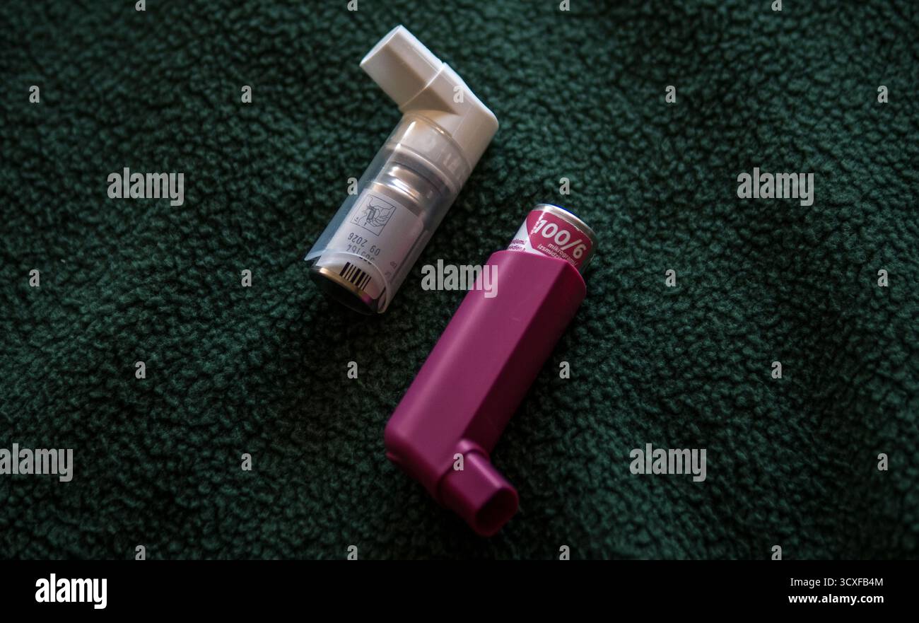 Nahaufnahme von zwei Asthma-Inhalatoren, einer rosa und einer weiß, auf einer dunkelgrünen texturierten Stoffoberfläche platziert.symbolisiert Gesundheit, Medizin. Stockfoto
