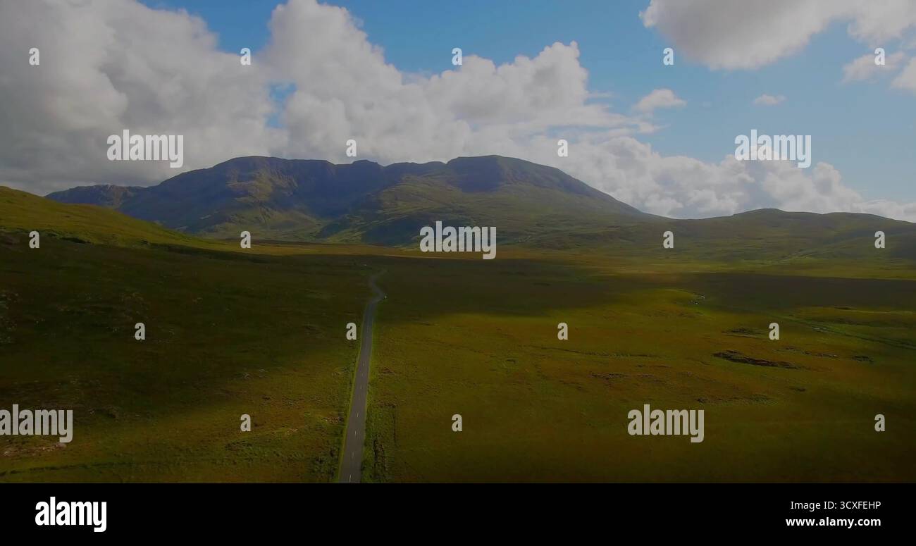 Durch schmale, einspurige asphaltierte Straße, die durch grasbewachsene Ebenen zu weit entfernten Berggipfeln führt Stockfoto