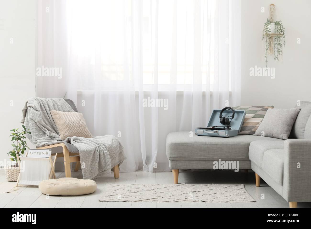 Stilvolles Wohnzimmer mit Sessel, Plattenspieler und Kopfhörern auf grauem Sofa Stockfoto