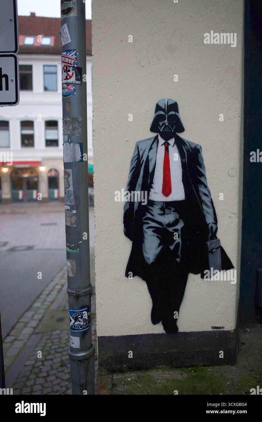 Flensburg, Schleswig-Holstein das Bild zeigt ein modernes Graffiti in Flensburg: Eine Figur im Anzug mit roter Krawatte und Aktentasche, deren Kopf die markante Maske von Darth Vader trägt. Das Kunstwerk befindet sich an einer Hauswand nahe einer Straßenecke und kombiniert Popkultur und Streetart auf humorvolle Weise. Unten rechts steht TABBY. Aufnahme vom 14.10.2025, Flensburg, *** Flensburg, Schleswig Holstein das Bild zeigt ein modernes Graffiti in Flensburg Eine Figur in einem Anzug mit roter Krawatte und Aktentasche, deren Kopf die markante Maske von Darth Vader trägt Stockfoto