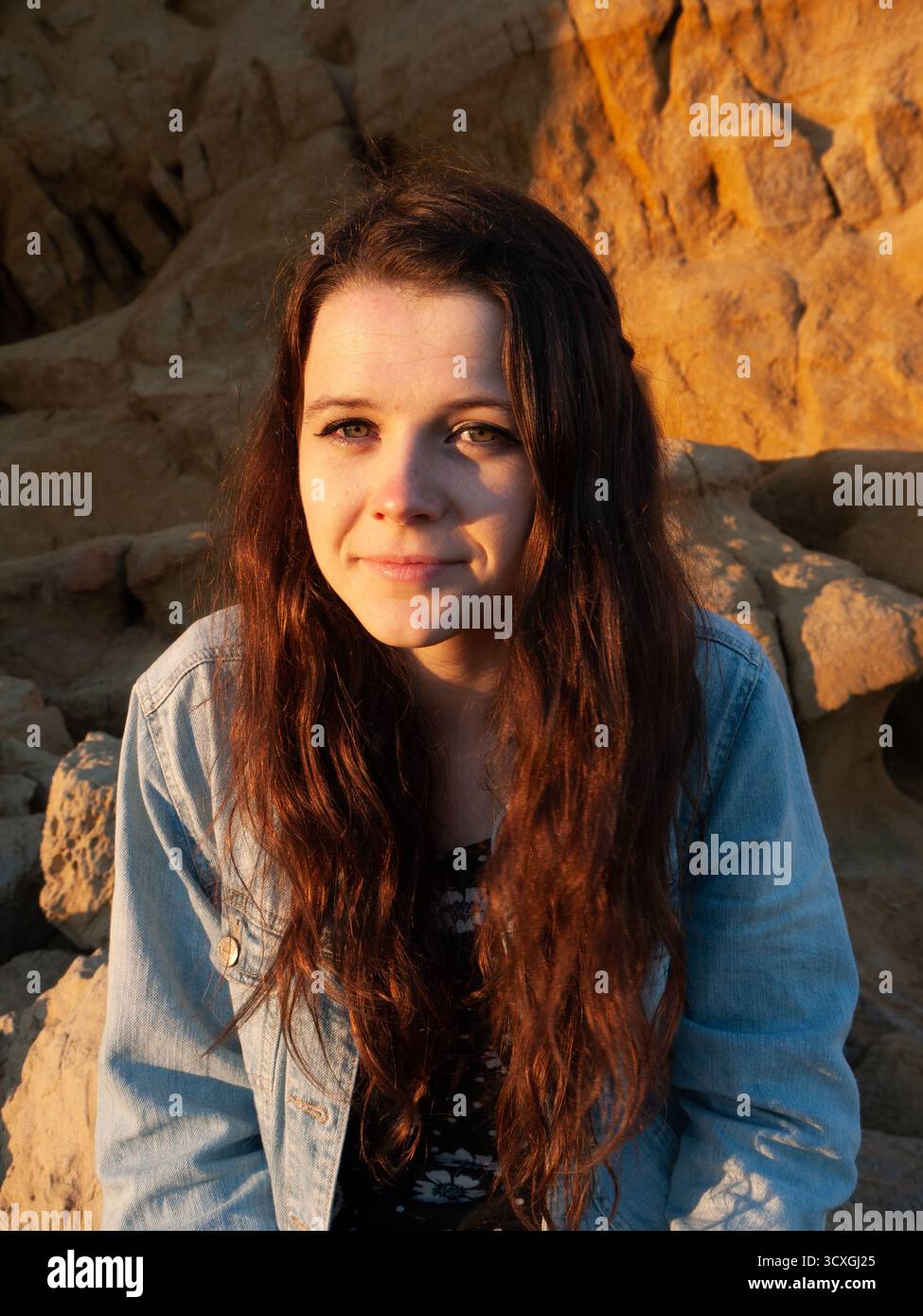 Junge Frau mit langen braunen Haaren im goldenen Abendlicht vor Kalksteinklippen Stockfoto