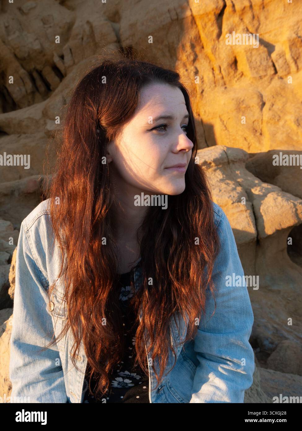 Junge Frau mit langen braunen Haaren im goldenen Abendlicht vor Kalksteinklippen Stockfoto