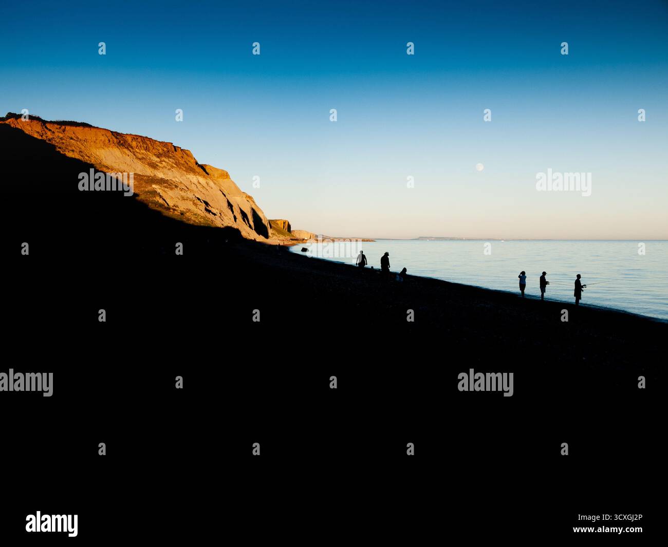 Silhouetten von Menschen am Strand bei Sonnenuntergang mit goldenen Klippen, Dorset Coast Stockfoto