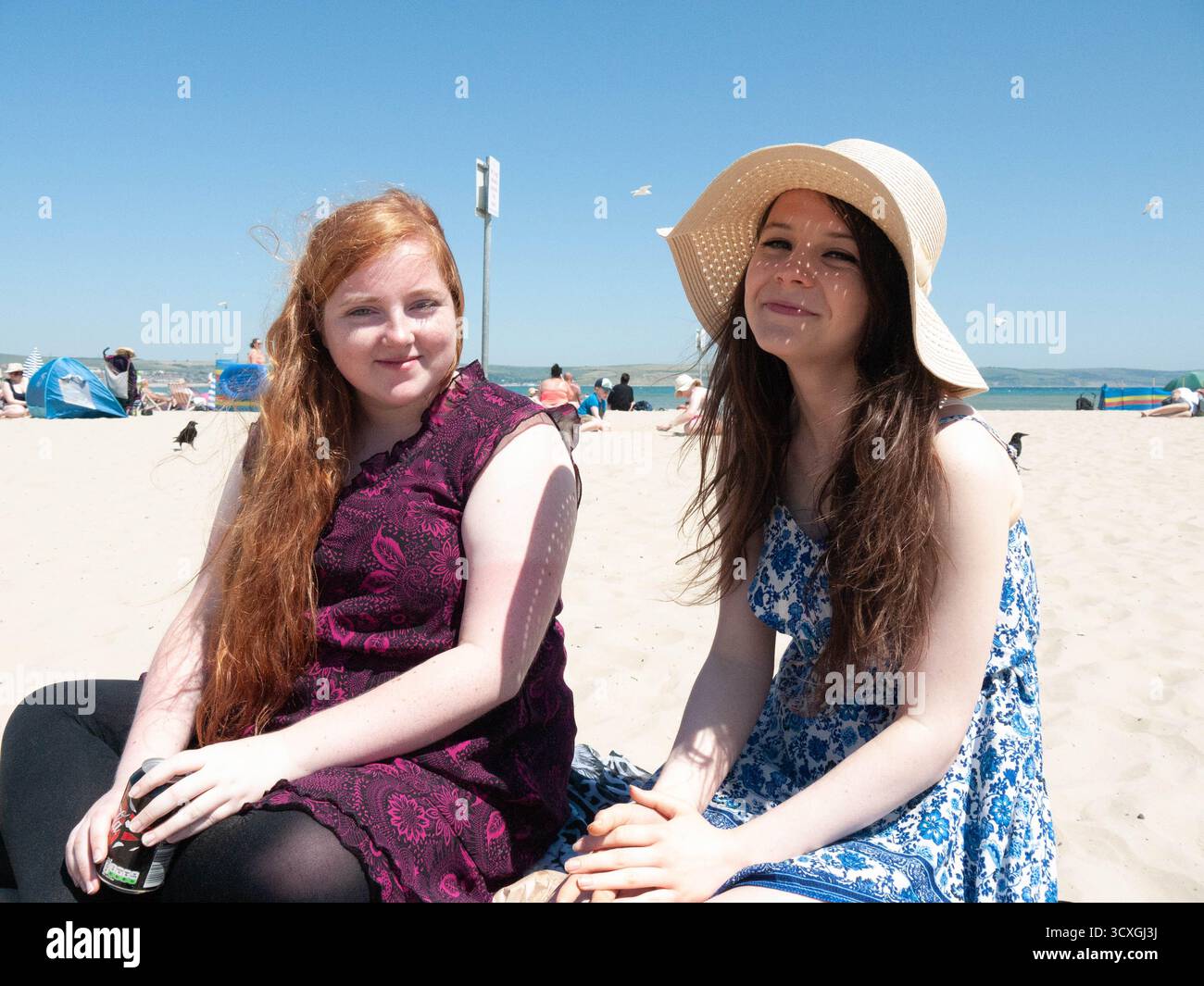 Zwei junge Frauen genießen einen sonnigen Tag am Dorset Beach mit Windschatten und blauem Himmel Stockfoto
