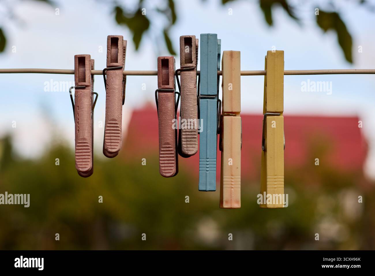Nahaufnahme von farbenfrohen, Vintage-Plastik-Kleiderschalen, die an einem Draht vor einem verschwommenen Hintergrund von Bäumen und einem Gebäude mit rotem Dach hängen. Stockfoto