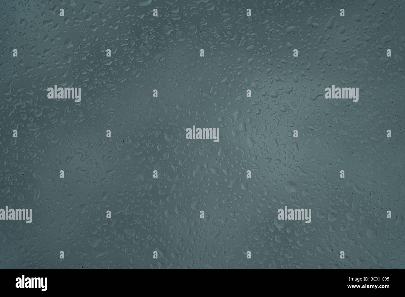 Regentropfen auf einer grauen Oberfläche erzeugen ein strukturiertes und stimmungsvolles abstraktes Muster. Stockfoto