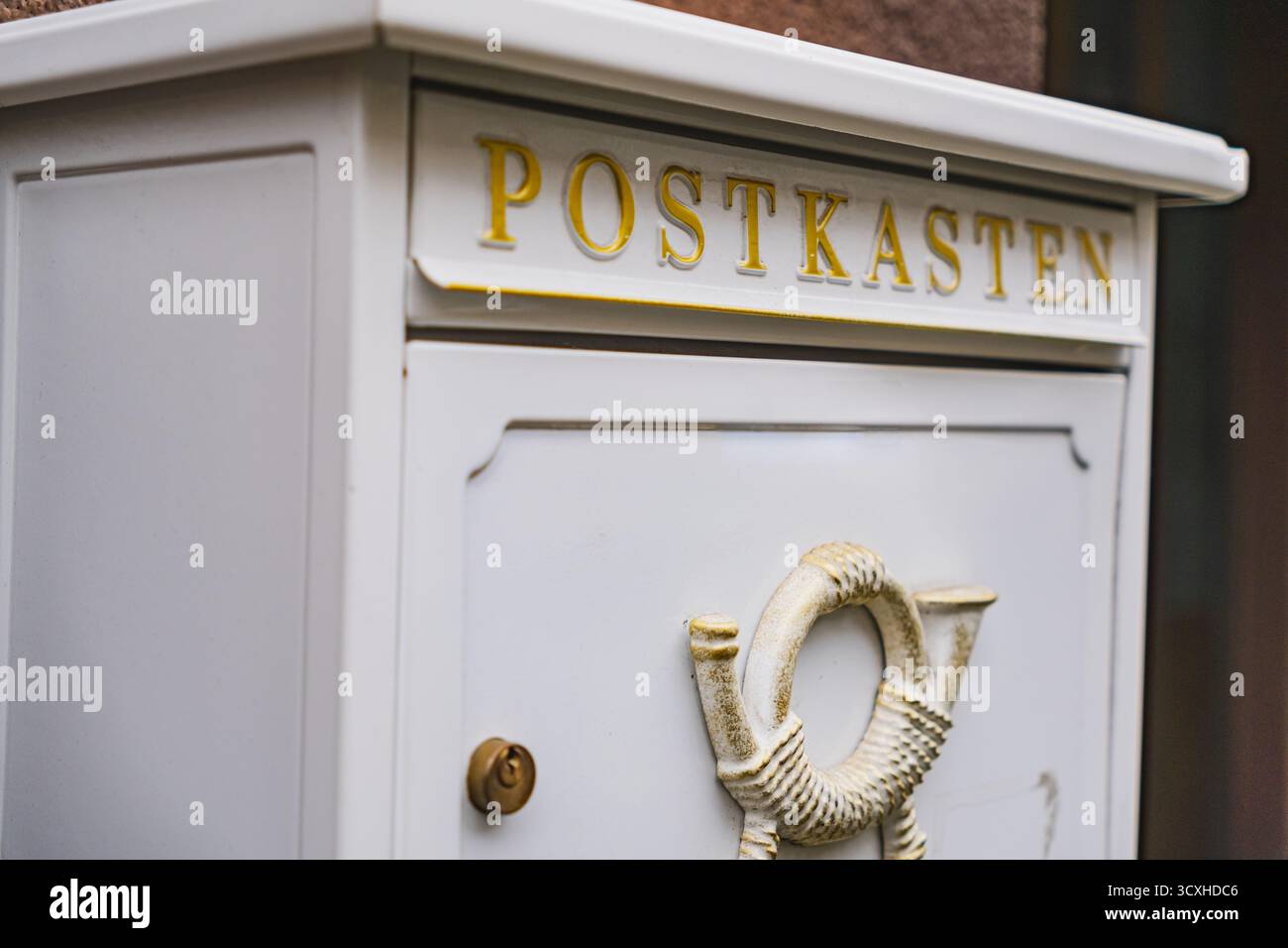 Weißer Briefkasten mit historischem Posthornrelief, das draußen an einer braunen Wand hängt Stockfoto