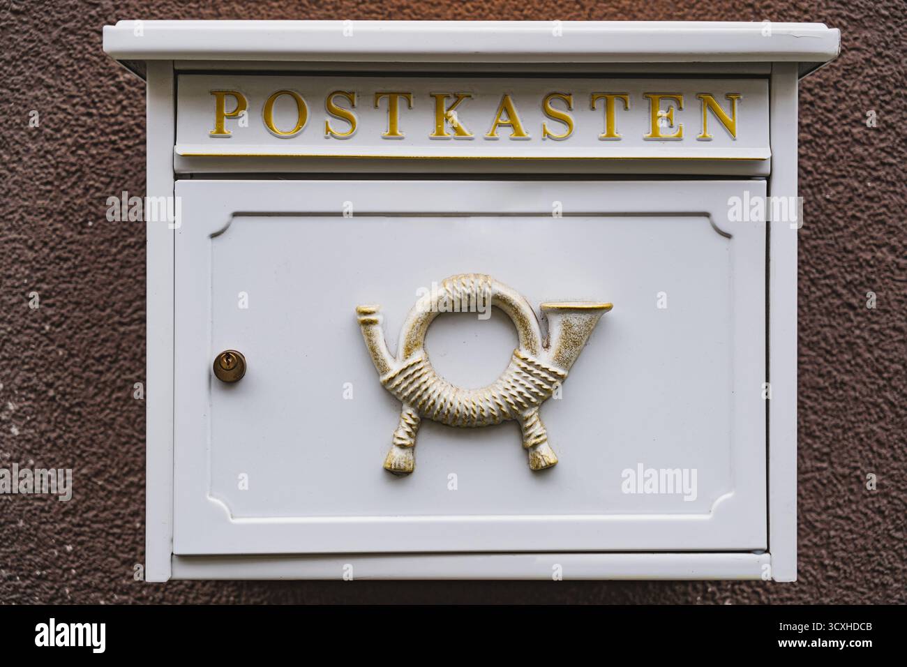 Weißer Briefkasten mit historischem Posthornrelief, das draußen an einer braunen Wand hängt Stockfoto