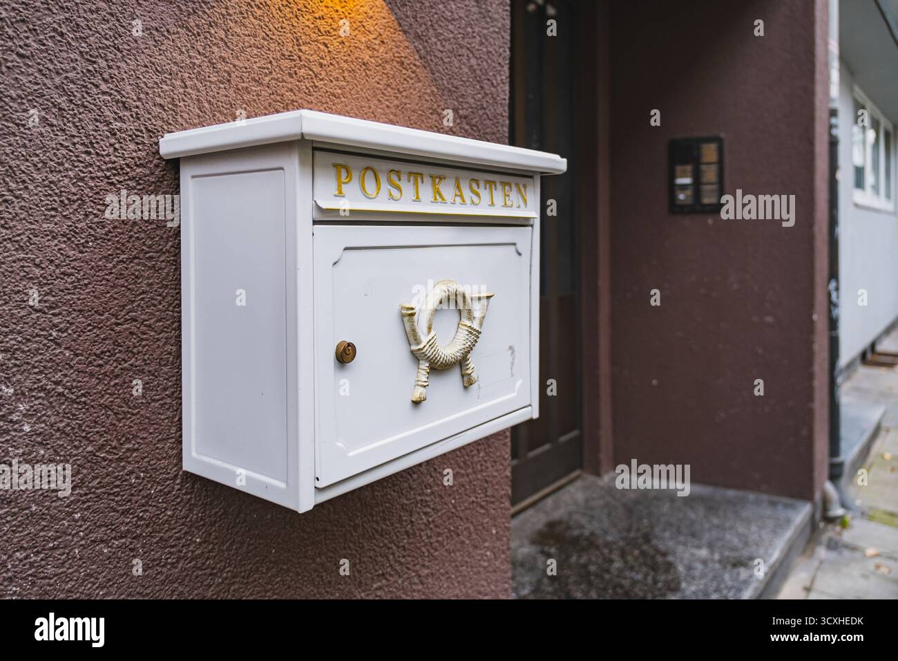 Weißer Briefkasten mit historischem Posthornrelief, das draußen an einer braunen Wand hängt Stockfoto