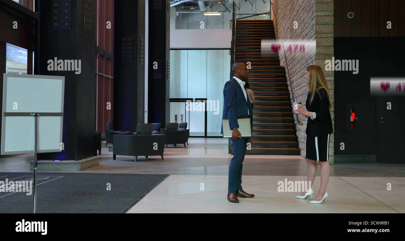 Stehende Kollegen in Anzügen, die eine Kaffeetasse und einen Laptop in der Lobby mit Schild halten Stockfoto
