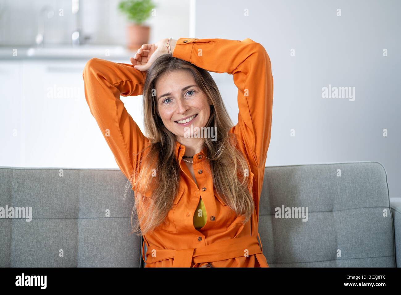 Fröhliche Frau mittleren Alters, die sich auf dem Heimsofa in einer Pose voller Entspannung und Selbstsicherheit ausruhen kann Stockfoto
