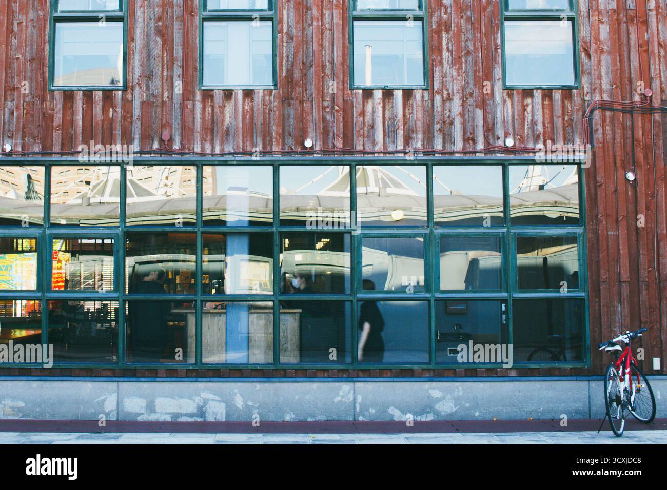 HAKODATE, JAPAN: Eine symmetrische, grafische Fassade eines rustikalen roten Holzlagers mit großen Fenstern, die den Himmel in der historischen Bucht reflektieren. Stockfoto
