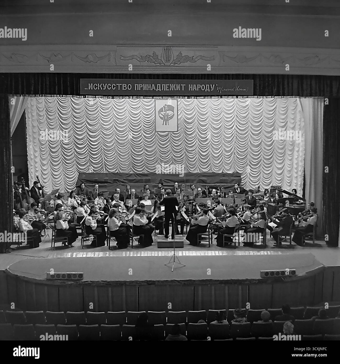 Ein Archivfoto aus dem Jahr 1984 zeigt ein Sinfonieorchester auf der Bühne des Artem Palastes der Kultur in Sloviansk, Ukrainische SSR. Ein Dirigent führt die Musiker vor einem Publikum, das im Saal sitzt. Über der Bühne zeigt ein prominentes Banner den klassischen leninistischen Slogan: „Kunst gehört dem Volk“. Die Szene fängt das reiche kulturelle Leben einer typischen sowjetischen Industriestadt ein. Dieses Bild ist ein wertvolles Dokument der Kunst und Ereignisse der Gemeinschaft in einem friedlichen Donbass vor dem Krieg Stockfoto