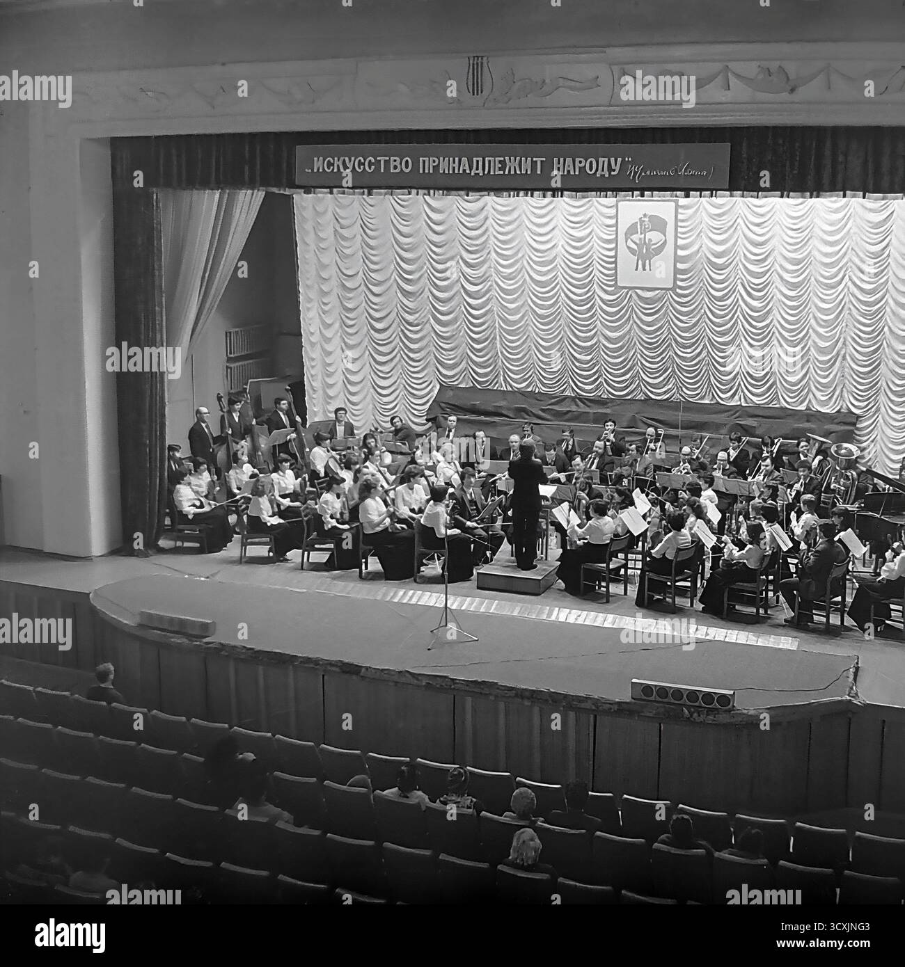 Ein Archivfoto aus dem Jahr 1984 zeigt ein Sinfonieorchester auf der Bühne des Artem Palastes der Kultur in Sloviansk, Ukrainische SSR. Ein Dirigent führt die Musiker vor einem Publikum, das im Saal sitzt. Über der Bühne zeigt ein prominentes Banner den klassischen leninistischen Slogan: „Kunst gehört dem Volk“. Die Szene fängt das reiche kulturelle Leben einer typischen sowjetischen Industriestadt ein. Dieses Bild ist ein wertvolles Dokument der Kunst und Ereignisse der Gemeinschaft in einem friedlichen Donbass vor dem Krieg Stockfoto