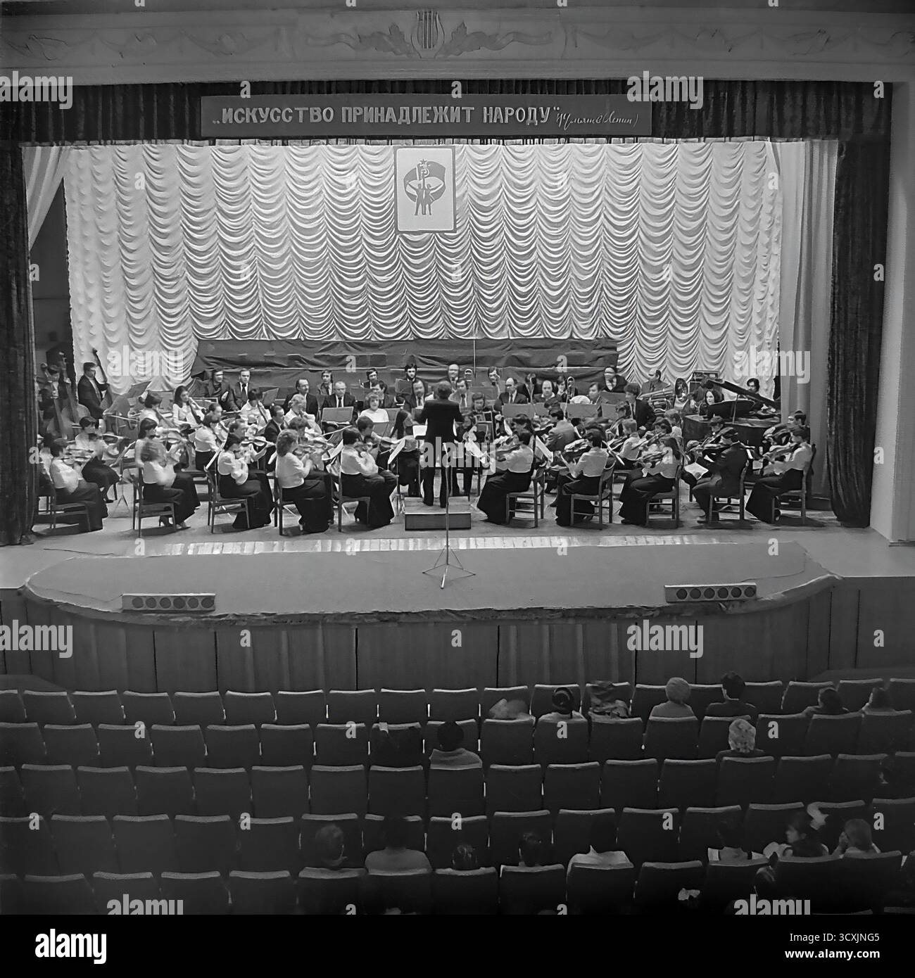 Ein Archivfoto aus dem Jahr 1984 zeigt ein Sinfonieorchester auf der Bühne des Artem Palastes der Kultur in Sloviansk, Ukrainische SSR. Ein Dirigent führt die Musiker vor einem Publikum, das im Saal sitzt. Über der Bühne zeigt ein prominentes Banner den klassischen leninistischen Slogan: „Kunst gehört dem Volk“. Die Szene fängt das reiche kulturelle Leben einer typischen sowjetischen Industriestadt ein. Dieses Bild ist ein wertvolles Dokument der Kunst und Ereignisse der Gemeinschaft in einem friedlichen Donbass vor dem Krieg Stockfoto