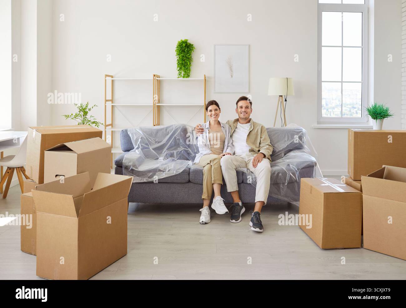 Lächelnde Pärchen, die sich auf dem Sofa entspannen und die Kartons auf dem Boden stapeln Stockfoto