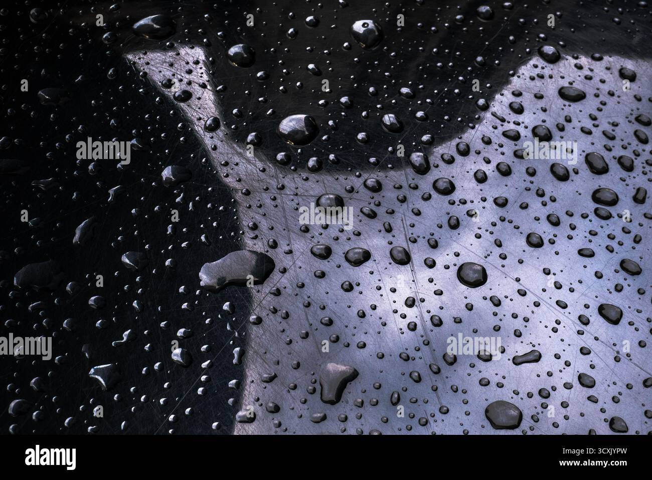 Stark bearbeitetes Bild von Tropfen auf zerkratzter, glänzend schwarzer Textur Stockfoto