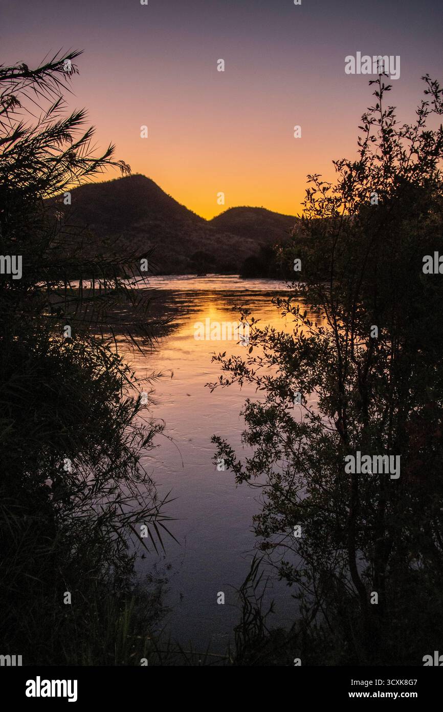 Violett-goldener Sonnenuntergang über dem stillen Wasser über den Epupa Falls zwischen Namibia und Angola. Stockfoto