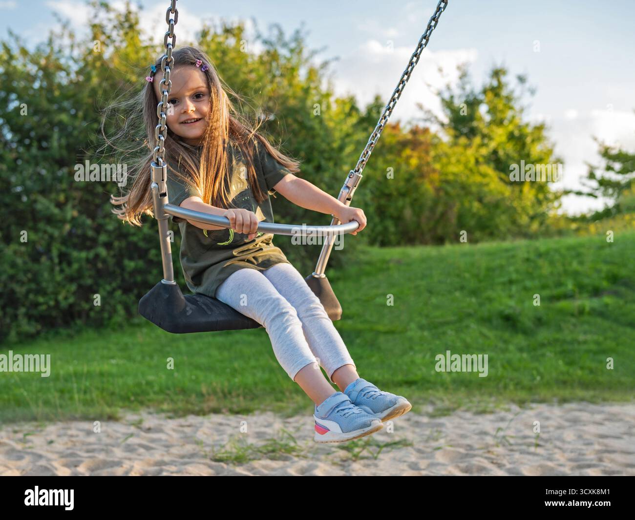 Glückliches Kleinkind, das einen sonnigen Tag auf einer Schaukel im Park, Kinderfreude und Outdoor-Spaß im Herbstlicht genießt. Stockfoto