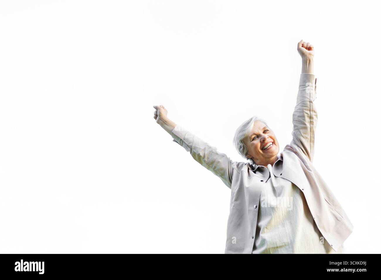 Glückliche ältere Frau mit grauem Haar, die die Arme vor Freude hebt, selbstbewusst vor weißem Hintergrund lächelt, das Leben, die Positivität, die Freiheit und aktiv feiert Stockfoto