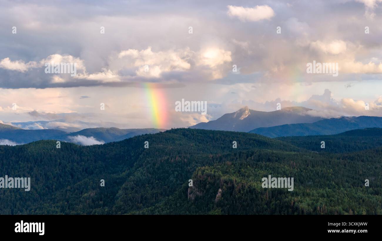 Nach dem Sommerregen taucht ein lebhafter Regenbogen über den bewaldeten Bergen auf Stockfoto