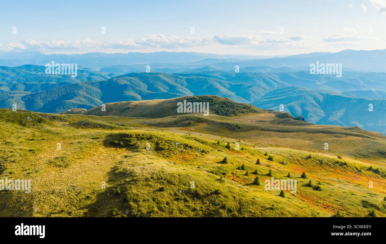 Heller Blick aus der Vogelperspektive auf sanfte grüne Berge und entfernte Waldkämme Stockfoto