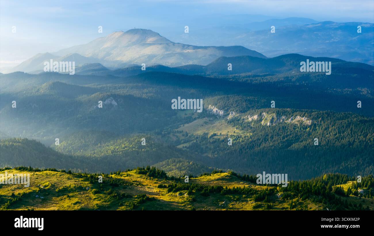 Schichten von Bergen und Waldtälern, die von der Sonne am frühen Morgen sanft beleuchtet werden Stockfoto
