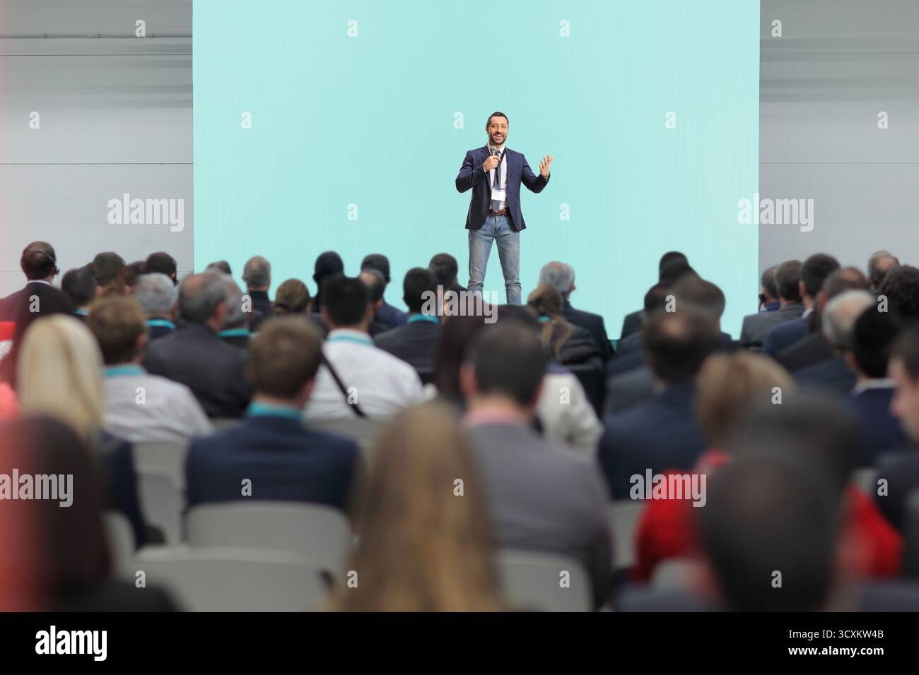 Mann, der ein Mikrofon hält und vor Publikum auf der Bühne spricht Stockfoto