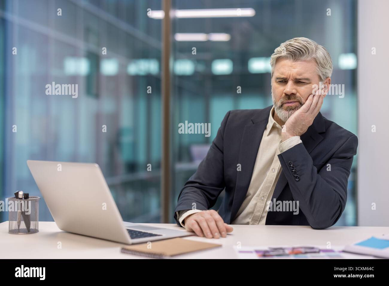 Reifer erfahrener Geschäftsmann, der am Arbeitsplatz krank ist, an Zahnschmerzen leidet und Hand an Gesicht hält Stockfoto