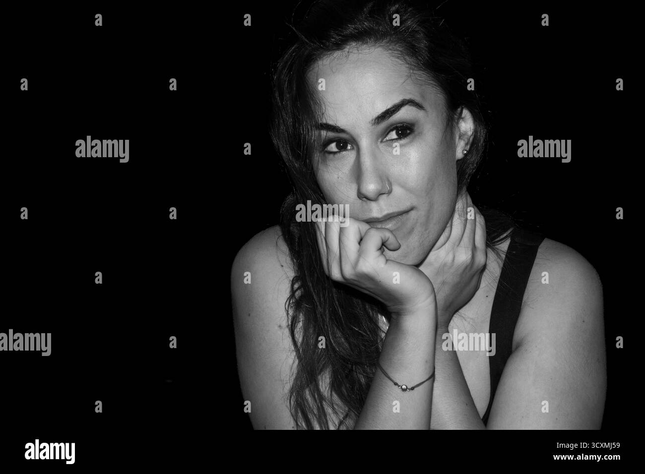 Frau, die einen persönlichen Gedanken mit nachdenklichem Ausdruck vor dunklem Hintergrund in Betracht zieht Stockfoto