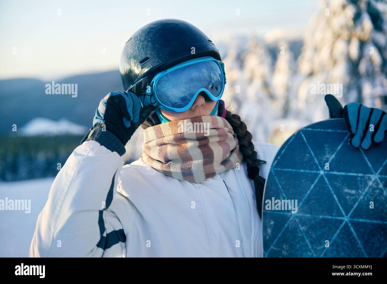 Porträt einer Frau, die ein Snowboard hält und Skibrille trägt. Skibrille Von Snowboardern Mit Dem Spiegelbild Der Verschneiten Berge. Stockfoto