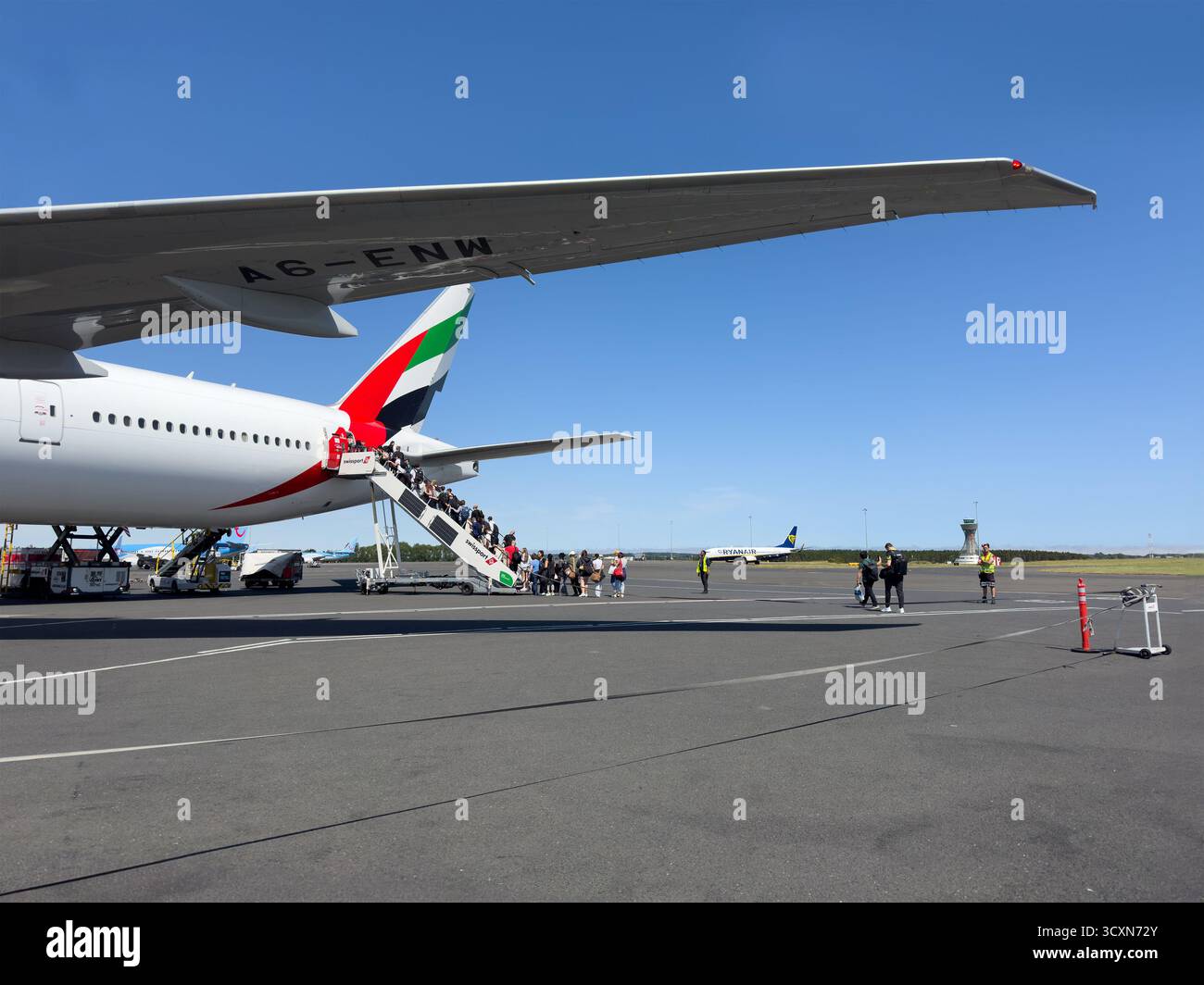 Passagiere, die die hintere Türtreppe eines Emirates-Flugzeugs auf dem Asphalt am blauen Himmel von Changi Singapur mit leuchtenden Schwanzfarben im Hintergrund besteigen - Smartphone-aufgenommenes Stockfoto
