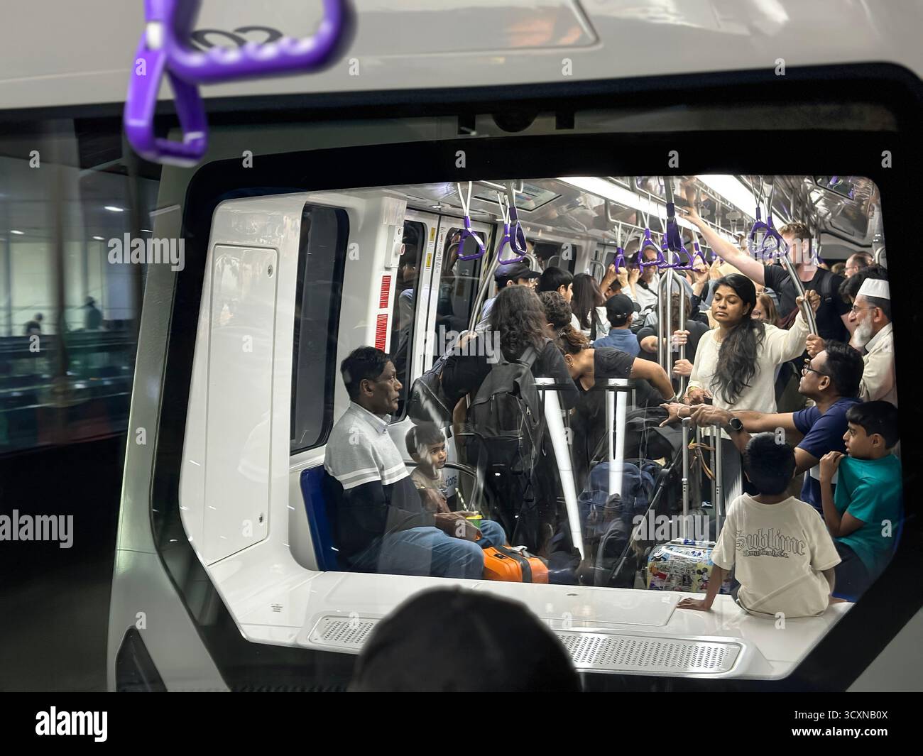 Ein überfüllter dubai DXB Airport Shuttle Zug mit verschiedenen Passagieren, einige sitzen und andere stehen während der Fahrt an Griffen - Smartphone-aufgenommenes Stockfoto