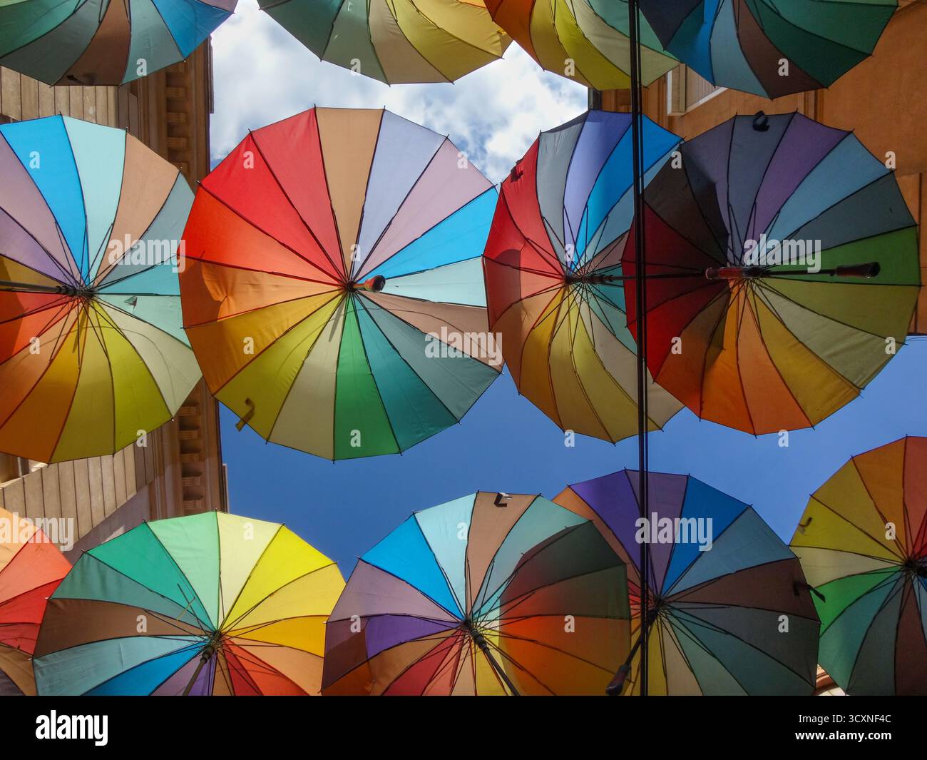 Bunte Sonnenschirme hängen an einem sonnigen Tag über einer engen Straße Stockfoto
