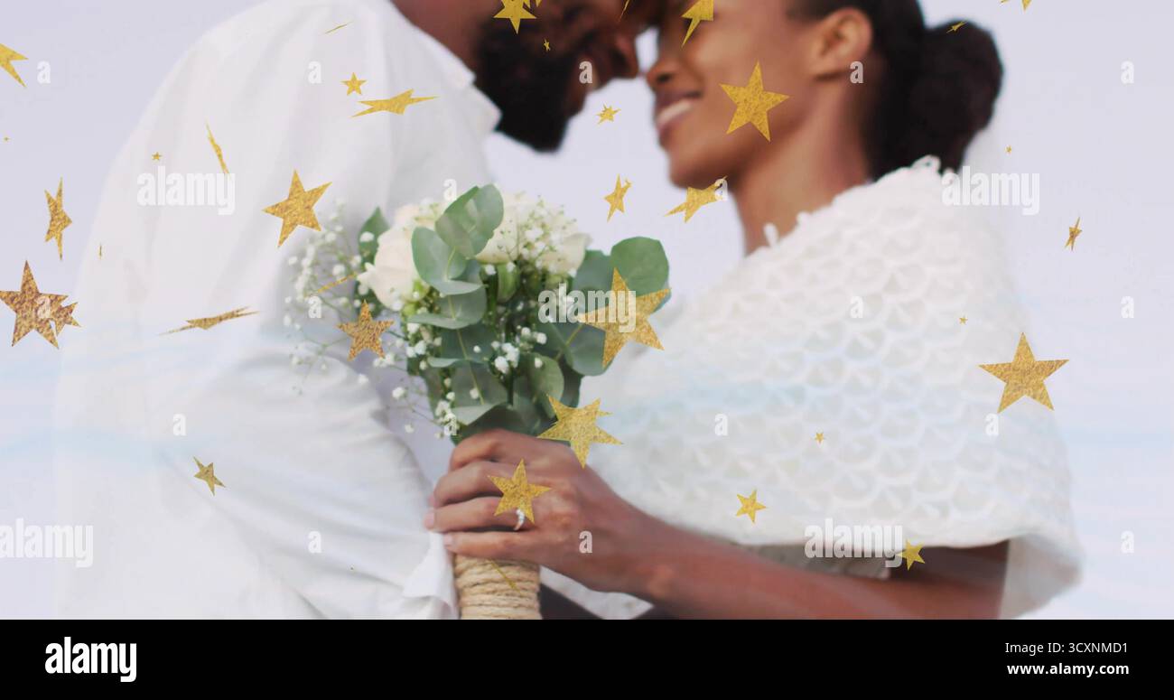 Ein stehendes Paar trägt weiß und teilt den Hochzeitsmoment am Meer mit Blumenstrauß und goldenen Sternen Stockfoto