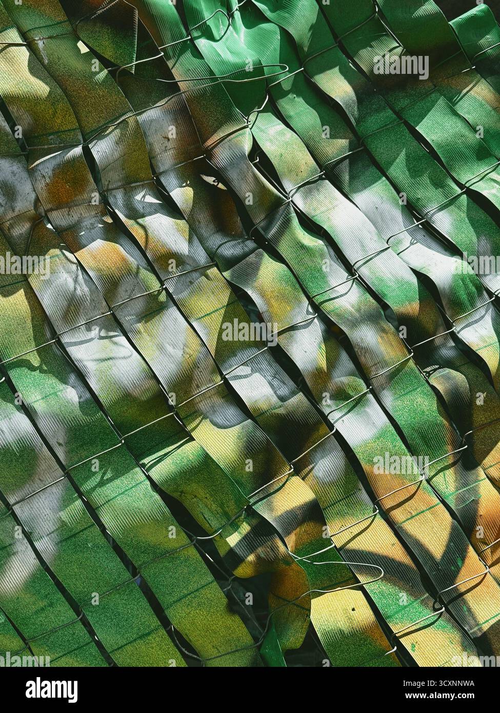 Nahaufnahme eines grün-braunen Tarnnetzes mit Sonnenlicht, das Schatten und Lichter auf der strukturierten Oberfläche erzeugt Stockfoto