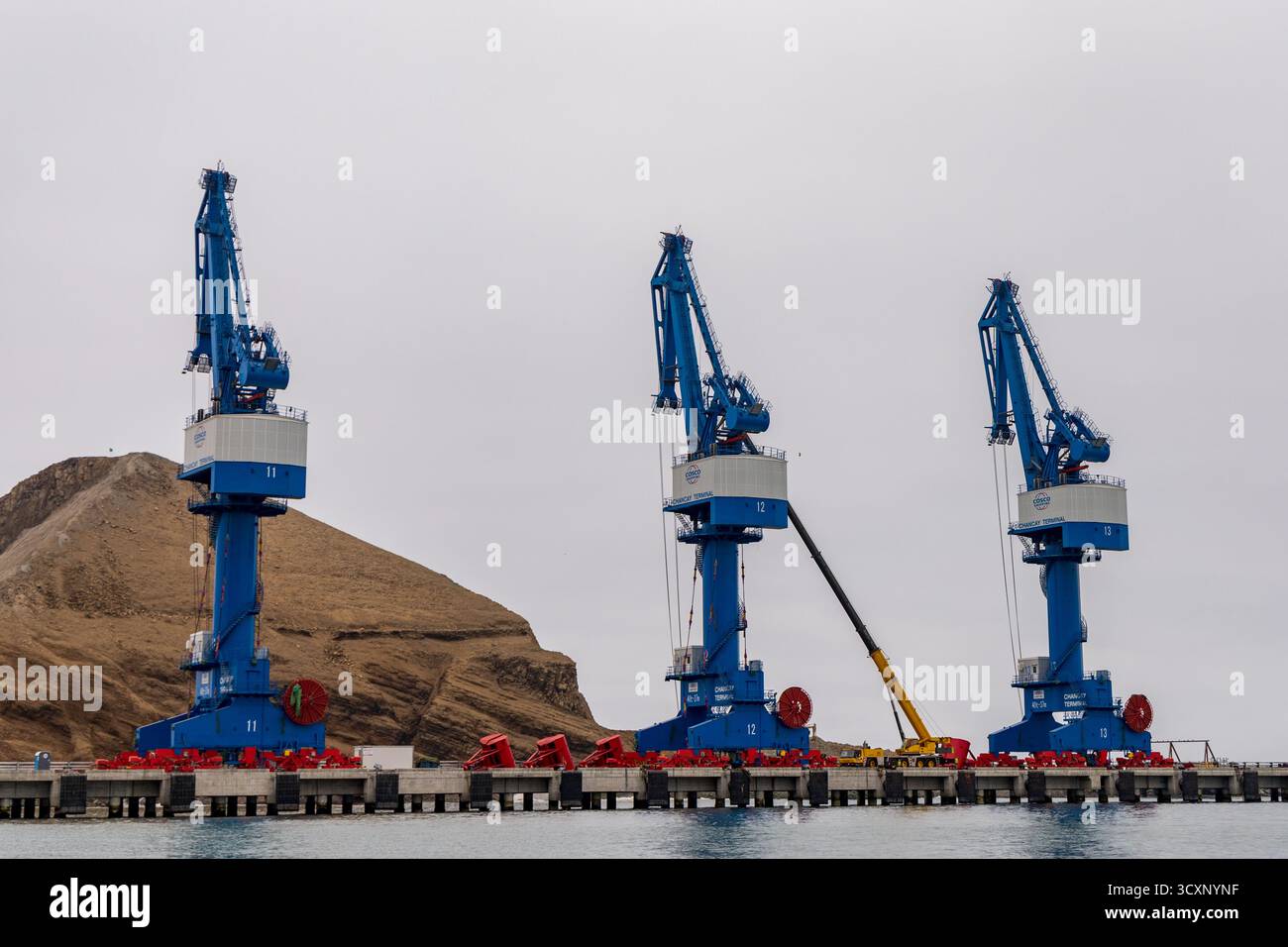 Chancay Mega Port. Drei blaue Kräne sind auf einem Dock in der Nähe eines Wassers. Die Kräne sind groß und blau und stehen in einer Reihe. Die Szene ist Stockfoto