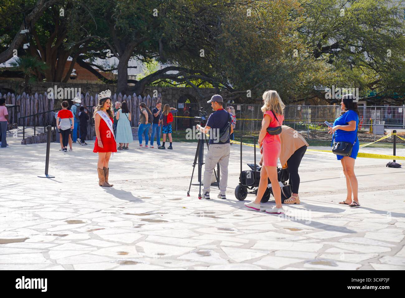 Ciara Davila, 2024 Miss Fiesta San Antonio Pageant Queen, wird von einem Videofilmer auf dem Gelände der Alamo Mission gefilmt, während Besucher in der Nähe spazieren gehen Stockfoto