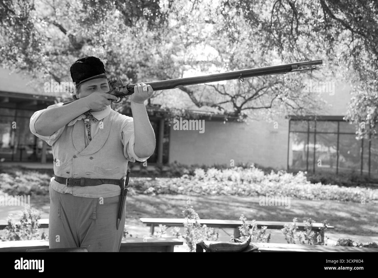 Schwarz-weiß-Bild eines historischen Reenactors, der während eines Geschichtsereignisses in der Alamo Mission eine Muskete anvisiert und das texanische Erbe zeigt Stockfoto