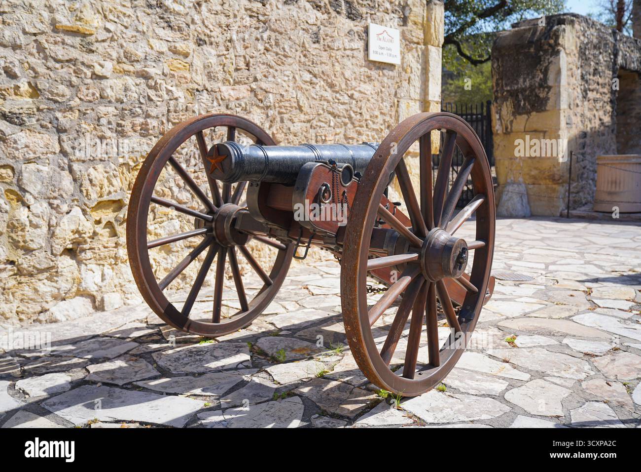 Historische Kanonen im Alamo in San Antonio, TX. Das erhaltene Artilleriestück, das auf Holzrädern montiert ist, steht an einer Steinmauer Stockfoto