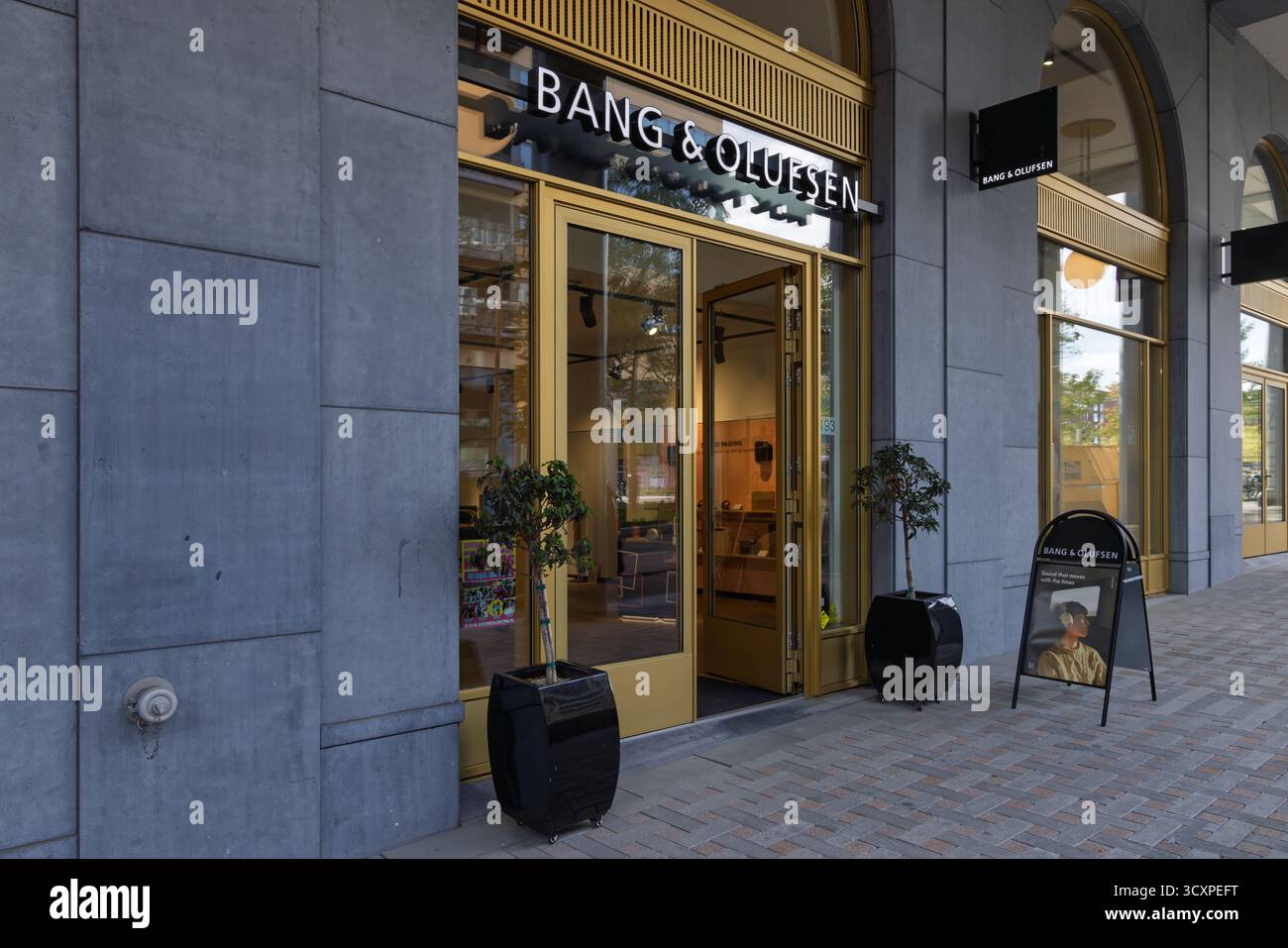 Das elegante Äußere eines Bang & Olufsen Stores mit goldenem Eingang, eingerahmt von schlankem grauem Stein und zwei dekorativen Pflanzgefäßen. Utrecht, Niederlande Stockfoto