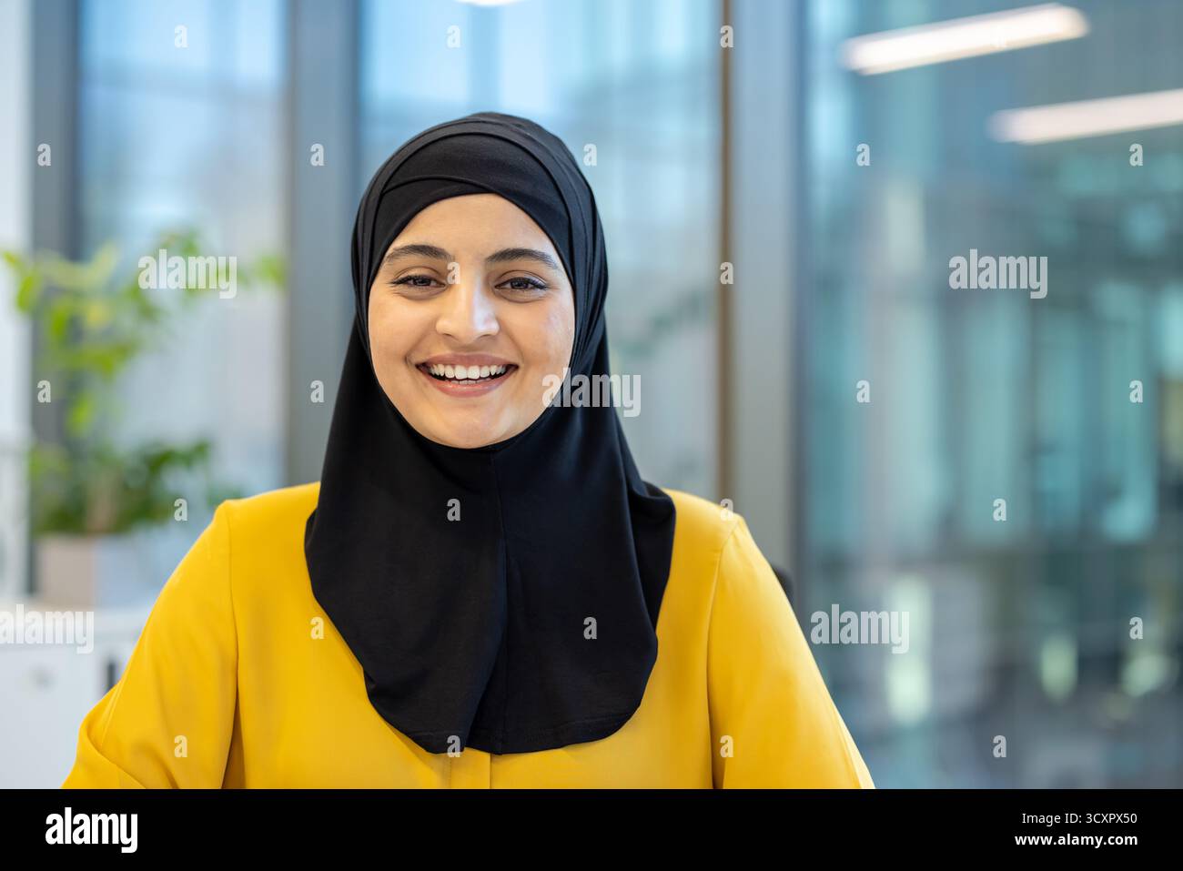 Muslimische Geschäftsfrau in Hijab und gelbem Blazer, die selbstbewusst lächelt, während sie in einem modernen Büroumfeld in die Kamera blickt und repräsentiert Stockfoto Muslimische Geschäftsfrau in Hijab und gelbem Blazer, die selbstbewusst lächelt, während sie in einem modernen Büroumfeld in die Kamera blickt und repräsentiert Stockfoto