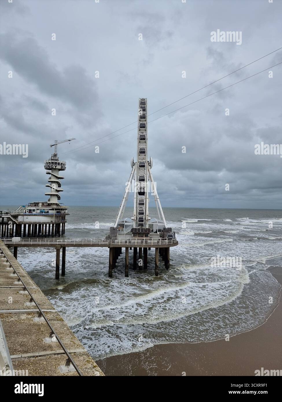 Seitenansicht des Piers Skyview: riesenrad in der Nordsee auf dem Pier in Scheveningen, Niederlande mit dunklen Wolken bei Herbstwetter; Bungy Jump - Smartphone-aufgenommenes Stockfoto