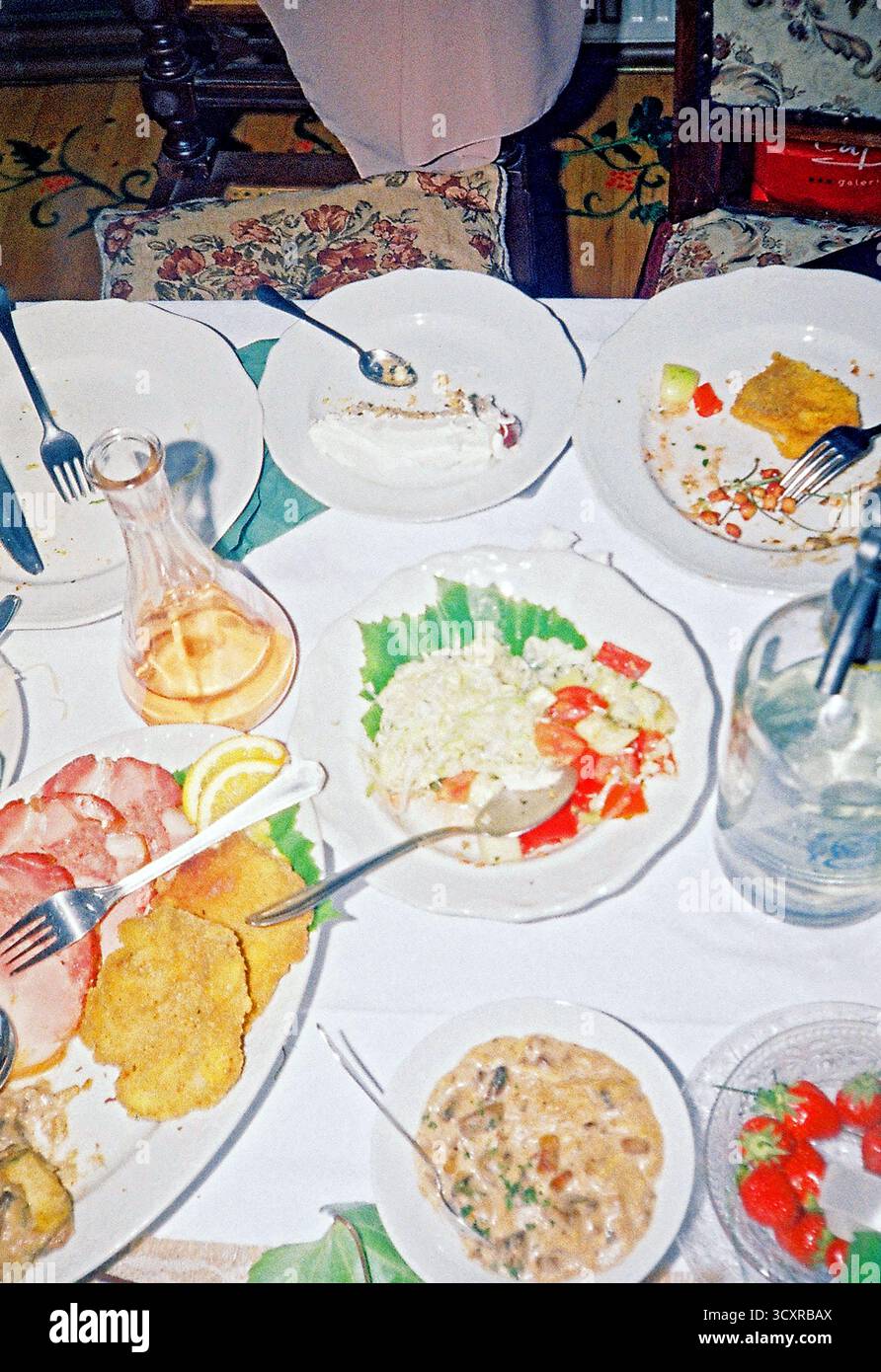 Ein üppiges Hochzeitsfest mit Russischem Salat, gebratenem Fleisch und Getränken auf einem überfüllten Tisch, fotografiert mit direktem Blitz auf Analogfilm. Stockfoto