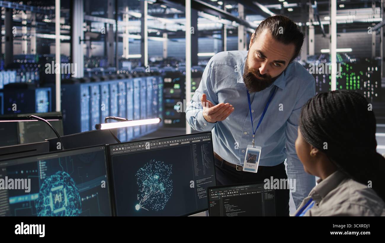 Der Serverraum-Manager gibt dem Mitarbeiter, der KI-Schulungsdatensätze verwaltet, Feedback. Teamleiter im Gespräch mit einem Techniker im Rechenzentrum, der den Systembetrieb überwacht, der neuronale Netzwerke unterstützt, Kamera A Stockfoto
